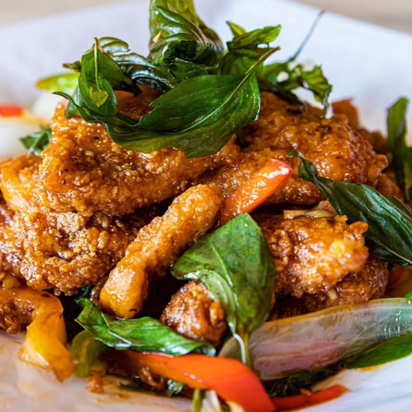 Close-up of golden-brown crispy Thai chicken with fresh green basil leaves and red peppers.