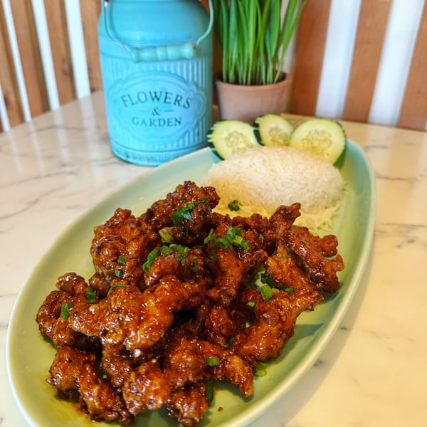 Thai fried chicken with rice and cucumber slices on a green plate, with a blue vase in the background.